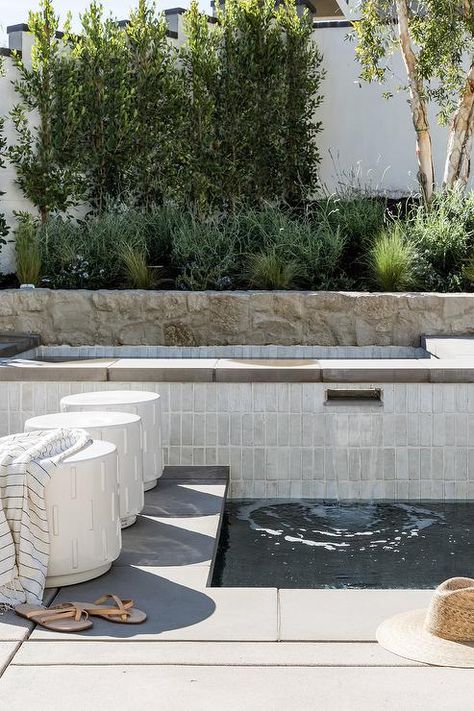 Spa features white stacked tiles and a pool waterfall. Backyard Idea On Hill, Precast Pool Coping, Stucco Pool Wall, Pure Salt Kitchen, Vertical Pool Tile, T Shaped Pool, Backyard Pool Remodel, Neutral Pool Tile, Subway Tile Pool Waterline