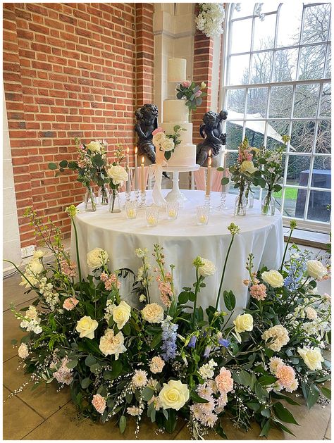 pastel pink, blue, ivory creams flower meadows at the bottom of a round cake table, bud vases on a cake table, beautiful cake table with flower meadows around it. Flower Meadows, Spring Flower Wreath, Wedding Flower Packages, Flower Meadow, Open Day, Wedding 2025, Wedding Cakes With Flowers, Flower Packaging, Cake Table