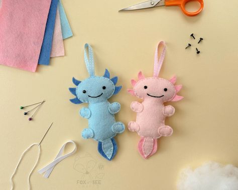 Sew your own Axel & Azul the Axolotls. Fox & Bee's Axolotl felt sewing kits are perfect for kids and adults of all ages and abilities - whether it's your first time sewing or you're an old hand, you'll love making these felt Axolotl decorations. In this kit you have everything you need to make your very own Pink & Blue Axolotls. Approx. Sizes (when made not including the ribbon): 85mm & 135mm each Inside your felt sewing kit * 40% Wool blend felt * Ribbons * Needle & Pins * Brads * Fluffy stuffi Axolotl Decorations, Axolotl Sewing Pattern, Hand Sewing Projects For Kids, Felt Axolotl, First Time Sewing, Felt Sewing Kit, Felt Sewing, Hand Sewing Projects, Felt Ideas