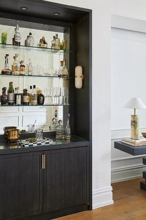 Black bar design features black cabinets with brass hardware and glass shelves on an antiqued mirror backsplash. Brass Bar Shelves, Black Wet Bar, Antiqued Mirror Backsplash, Brownstone Living Room, Glass Bar Shelves, White Bar Cabinet, Black Bar Cabinet, Bar Nook, Home Wet Bar