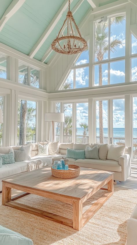 Coastal living room with ocean view, light blue decor, wooden coffee table, soft sunlight, and rustic chandelier for warmth. Living Room Florida Interior Design, Florida Homes Interior Design Coastal, Southern Beach House Decor, Minimalistic Beach House, Lake Interior Design, Coastal House Living Room, Ocean Theme House, Ocean Themed Living Room, Seaside Interior Design