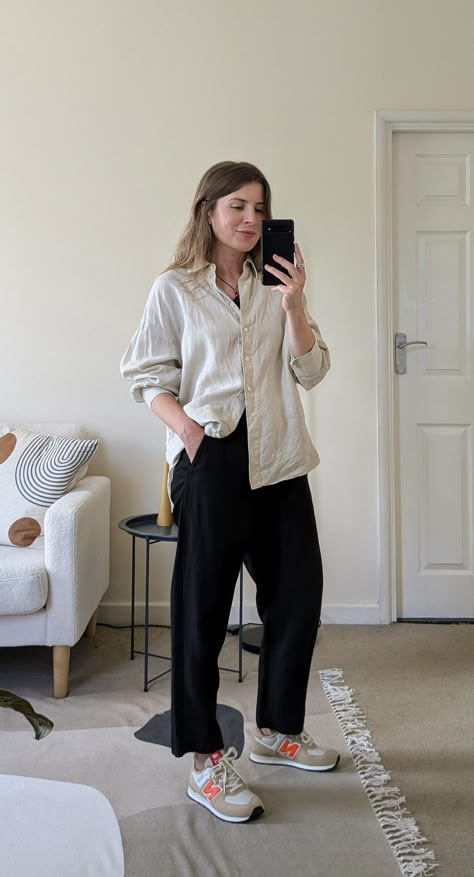 A woman stands in front of a mirror. She wears a black cord necklace, ecru oversized shirt with the sleeves pushed up, black cropped trousers and beige and orange New Balance sneakers. Crop T-shirt Outfits, Women’s New Balance 574 Outfit, New Balance Style Women Outfits, Black Pants And Sneakers Outfit, Oversized Outfits Summer, Cute Outfits With New Balance, Casual Black Trousers Outfit, Casual Summer Outfits With Sneakers, Nb 574 Women Outfit