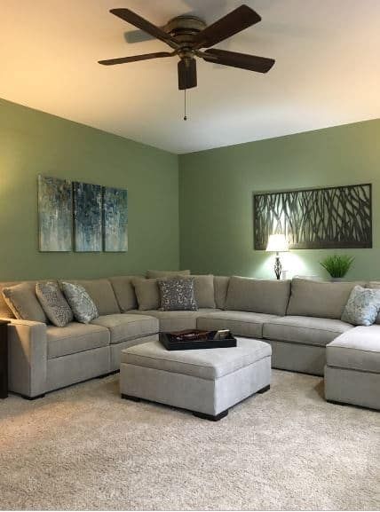 The gray carpeted flooring is a complement to the large gray L-shaped sofa that stands out against the green walls accented with wall-mounted artworks of tree silhouette. Green Walls Living Room, Sage Green Living Room, Green Living Room Decor, Living Room Wall Color, Walls Living Room, Room Wall Colors, Green Living Room, Room Green, Living Room Photos