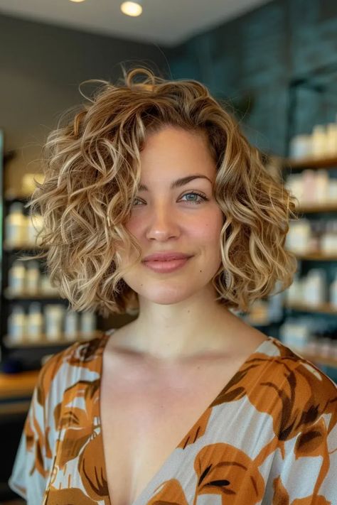 Smiling person with curly, shoulder-length hair in a floral blouse, standing in a modern store. Short Haïr Cut For Curly Hair Girl, Blonde Bob Curly Hair, Short Curly Womens Haircuts, Curly Bob Hairstyles Blonde, Neck Length Hair Curly, Short Haircuts For Curly Hair Round Face, Face Framing Curtain Bangs On Curly Hair, Thick Curly Bob, Thick Curly Hair Short