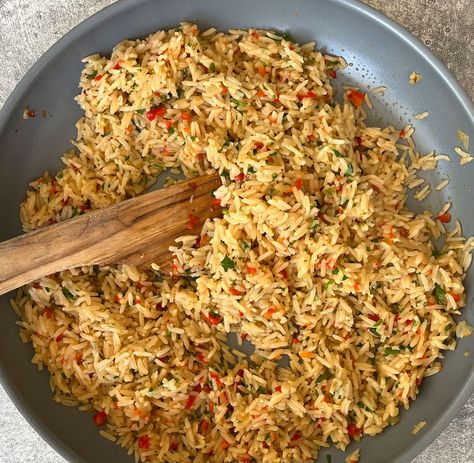 There is a large gray skillet with cooked rice, chopped onion, chopped red pepper, chopped fresh parsley, and minced garlic in it. There is a wooden spoon in the skillet. The skillet is on a light gray surface. Garlic Rice Pilaf, Rice Pilaf With Mushrooms, Steakhouse Rice Pilaf, Herbed Brown Rice, Japanese Steakhouse Fried Rice, Chile Relleno Casserole Recipe, Longhorn Steakhouse, Rice Pilaf Recipe, Chicken Piccata Recipe