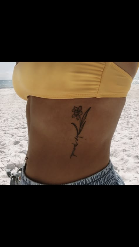 Daffodil tattoo on ribs, be proud Daffodil Tattoo Ribcage, Daffodil Tattoo On Hand, Daffodil Tattoo Ribs, Daffodil Tattoo Thigh, Daffodil Rib Tattoo, Birth Flower Tattoos On Ribs, Daffodil Tattoo With Date, Daffodil Tattoo With Name, Daffodil With Name Tattoo