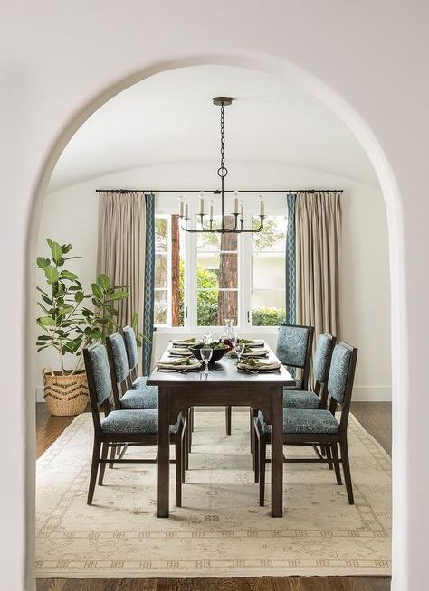 Cream and blue Mediterranean style dining room features blu dining chairs backed on a cream wool rug around a dark wood dining table lit by an iron chandelier. Mediterranean Dining, Mediterranean Dining Room, Spanish Modern, Mediterranean Style Home, Bungalow Homes, Mediterranean Style Homes, Mediterranean Home Decor, Bungalow Style, Spanish Style Homes