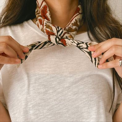 Close up of model tying a bandana around the neck. Ways To Fold Bandanas, Bandana With Outfit, Wearing A Bandana Around Neck, How To Style Bandana Around Neck, How To Tie Handkerchief Around Neck, Neck Scarf Tie, How To Tie Neck Bandana, How To Tie A Western Scarf, Tying A Bandana Around Neck