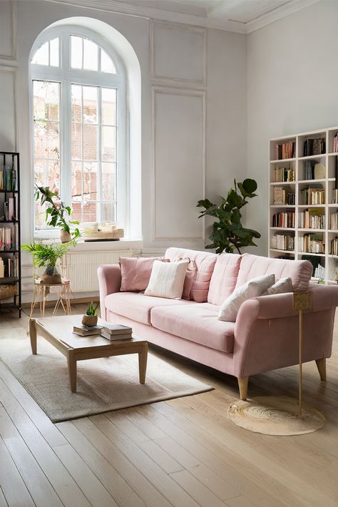 Calm Retreat • The room features an arched window that bathes it in natural light • A dusty pink sofa adds a gentle pop of color to the neutral palette • Wooden coffee table with clean lines sits atop a natural fiber rug • A tall, leafy indoor plant brings a refreshing energy to the corner • White bookshelves brimming with books suggest a love for literature • Muted tones and subtle textures throughout the room evoke a sense of peace Pink Sofa Aesthetic, Dusty Pink Sofa, Pink Aesthetic Home, Soft Pink Aesthetic, Natural Fiber Rug, White Bookshelves, Aesthetic Home Decor, Pink Sofa, Stylish Living Room