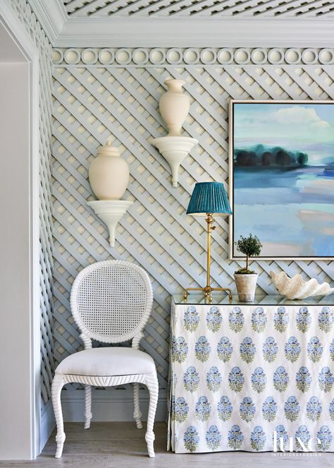 A Perennials material covers a side chair from Hive Home, Gift & Garden in the dining room, where general contractor John Prendergast fabricated the lattice. The custom console, covered with a linen Lisa Fine Textiles skirt, holds a Hudson Valley Lighting lamp. Hannah Bureau artwork completes the scene. Lisa Fine Textiles, Courtney Davis, Benjamin Moore Cloud White, Lattice Wall, Terrace Floor, Custom Consoles, Morning Room, Lighting Lamp, Design Salon