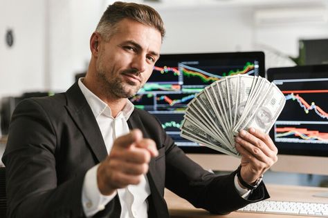 Premium Photo | Image of pleased businessman 30s wearing suit holding money fan while working in office with graphics and charts on computer