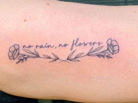 Script tattoo in font Artifact with two wispy flowers underneath. Tattoo reads “no rain, no flowers”. Flower Quote Tattoos For Women, Lower Bicep Tattoo Women Words, No Rain No Flowers Wrist Tattoo, Writing With Flower Tattoo, It’s Ok Flower Tattoo, Flowers Surrounding Words Tattoo, Flower Words Tattoo, Word Tattoo With Flowers Around It, Flowers Need Time To Bloom Tattoo