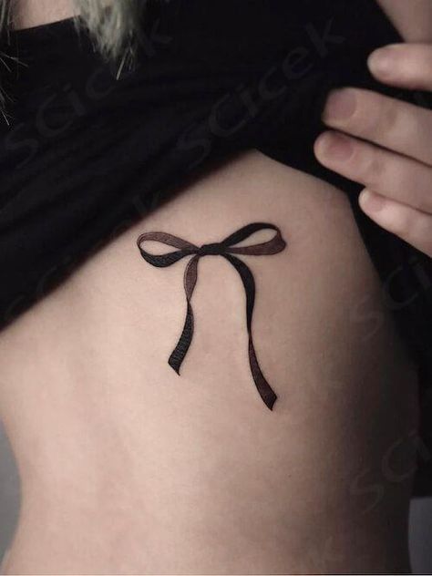 Explore bow tattoo meaning. Discover the symbolic meaning behind bow tattoos and get inspired with our collection of unique bow tattoo designs and bow tattoo ideas. Lace Bows Tattoo, Bow Bracelet Tattoo, Goth Bow Tattoo, Bow Tattoo Aesthetic, Cute Bow Tattoos, Bow Back Tattoo, Gothic Bow Tattoo, Finger Bow Tattoo, Bow Finger Tattoo