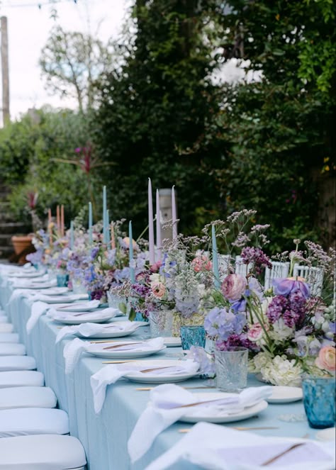 Light pastel blue table cloth with alternating clear and blue drinking glasses. Low and whimsical floral centerpieces mixed with blue, purple and peach candlesticks. Lavender And Blue Wedding, Purple Table Settings, Blue Table Cloth, Blue Wedding Table, Purple Wedding Tables, Light Purple Wedding, Blue Drinking Glasses, Blue Purple Wedding, Purple And Peach