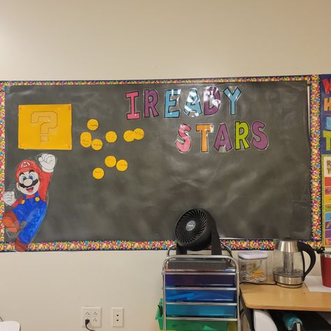 This iready board has a black background with a pixel themed border. The words Iready stars are in big letters while also have Mario jumping and hitting a question box. Each time a student gets an 85% or higher on an Iready lesson they write their name on a coin and put it on the board. Mario Jumping, Question Box, Student Of The Week, Big Letters, Kindergarten Classroom, A Student, Super Mario, Classroom Ideas, Black Background