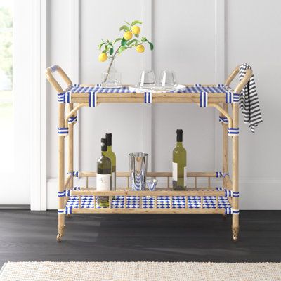 This bar cart offers a stylish way to serve up drinks and snacks, whether you're hosting a gathering or enjoying a relaxing evening at home. The solid bamboo frame features a light brown finish, while the top and bottom shelves showcase woven blue-and-white acrylic detailing for a coastal vibe in your space. With four wheels and two handles, this cart is easy to move around, and the included towel bar ensures you always have a cloth handy for spills. The cart's 50 lbs. weight capacity allows for Bar Cart Wood, Bar Corner, Wood Bar Cart, Relaxing Evening, Serving Cart, The Company Store, Bar Art, Florida House, Bamboo Frame