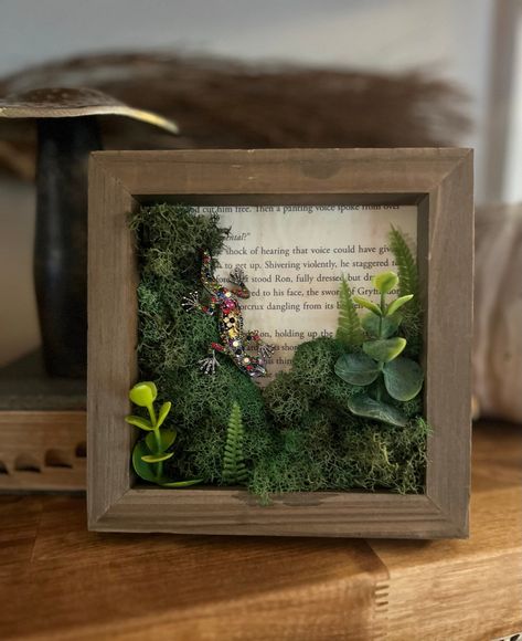 "We start by applying a hand aged page from the stories of a famous boy wizard, then add moss and greenery, then perfectly place the jeweled gecko.  Each item is carefully handmade to create a wonderfully whimsical piece. Dimensions: 6\" x 6\" x 1\"" Small Shadow Box Ideas Diy, Moss Crafts Diy, Framed Moss Wall Art, Moss Diorama, Whimsical House Decor, Moss Picture Frame, Moss Board, Moss Crafts, Tolkien Wedding