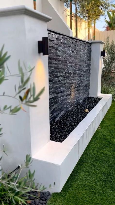 The dramatic black and textured finish creates an extraordinary visual appeal, perfect for those looking to add a bold touch to their interiors. Pin this for your next bold project! Designer: @jonathanbonillas Yard Wall Design Outdoor, Home Outside Wall Design, Outside Wall Decor Front Yards, Outdoor Waterfalls Backyard, Outdoor Fountains Landscape, Wall Design Outdoor, Modern Landscape Design Front Yard, Waterfall Outdoor, Backyard Fountain