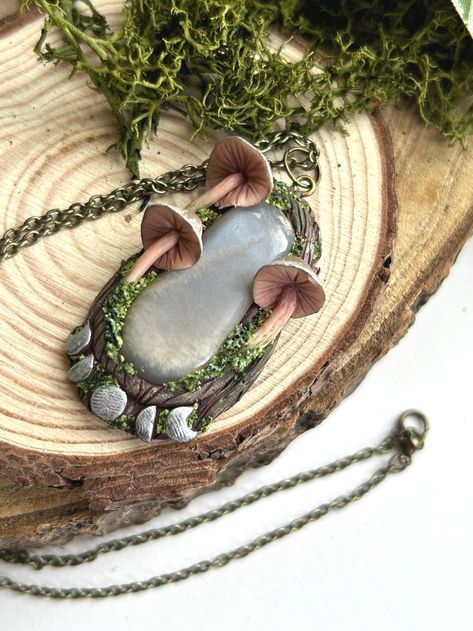 A magical mushroom handmade pendant with silver moon phases and a black moonstone crystal! Sculpted with polymer clay, this witchy pendant has a woodland bark texture background, made to look like it has been created by ancient witchy faes in the woods. This pendant also features 3 hand sculpted mushrooms, each with an earthy brown colour cap which has silver metallic streaks. This pendant also has silver moons at the bottom, creating the phases of the moon underneath the black moonstone crystal