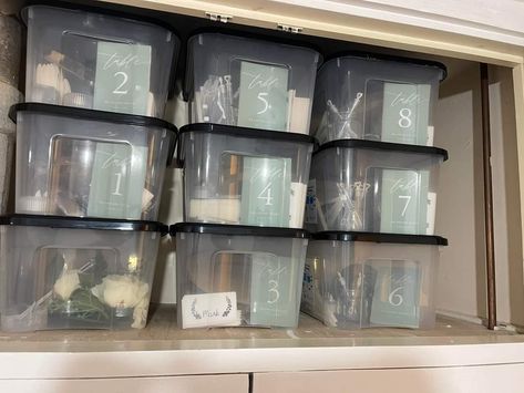 Storage bins neatly arranged by table number with the contents inside intended for use on the tables at a wedding reception. Each box contains things such as artificial flowers, flower vases, candles, table number identifier, and whatever else they may want on the table associated with that number. Pictured above is nine clear boxes, stacked three boxes high and three boxes wide.  You can see the contents inside the clear boxes and the numerical table number associated with the contents inside! Organizing Wedding Decorations, Organize Wedding Decorations, Wedding Storage Ideas, Wedding Table Organization Bins, Wedding Decor Organization, Book Lovers Wedding, Wedding Planning Organizer, Shoe Box Storage, Wedding Setup