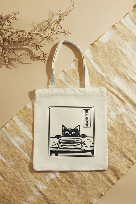 Our cute cat and fish design tote bags are made from cotton canvas material. This environment friendly tote bag is perfect for your daily use to carry essentials, groceries, or books. The cute Japanese style design brings a touch of cultural charm to your outings! The writing is a Japanese proverb and it translates "Trusting the cat to watch over the fish." which means it is obvious that the situation is dangerous.    - It is 100% cotton  - Environment friendly - Machine wash cold and inside out Unique Tote Bag Design, Simple Tote Bag Design, Grocery Bag Design, Cool Tote Bag Design, Cute Tote Bag Design, Tote Bag Inspo, Tote Bags Design, Tote Bag Design Ideas, Bag Design Ideas