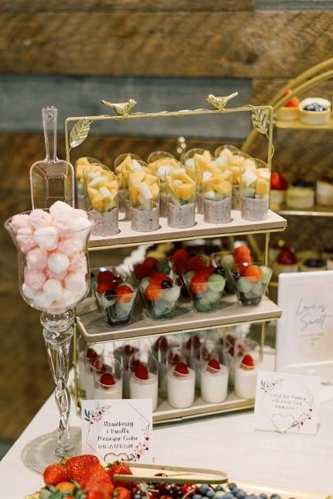 Styling a dessert display has never been this fanciful, so make use of a 3-tier rectangular gold cupcake stand tower. Its rustic design will absolutely balance the tall decorative clear glass pedestal candy jar placed adjacent to it. And don’t skip labeling your sweet treats as a thoughtful gesture to your guests using gold double-heart menu clips. This beautifully designed dessert display will truly work wonders for your family and friends. Gold Cupcake Stand, Event Decor Ideas, Party Decorations Table, Cake Stand Decor, Wooden Cake Stands, 3 Tier Cake Stand, Cupcake Stands, Glass Pedestal, Decorations Table