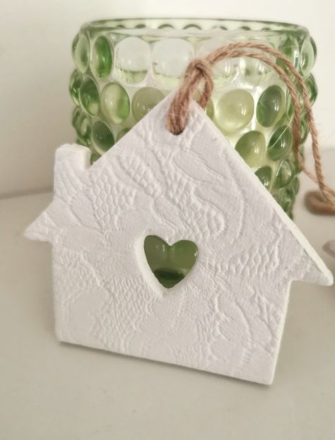 An air dry clay house shaped wall hanging. The front has been imprinted with a lace effect design and a heart punched out, the back is left blank. The house is then finished with a natural twine. Measurements: 3 inches x 3 inches. This would make a lovely keepsake for a new home owner. Air Dry Clay Houses, Air Dry Clay Ornaments Diy, Clay Draping, Das Clay, Modelling Ideas, Clay Gifts, Christmas Pottery, Clay Christmas Decorations, Clay Items