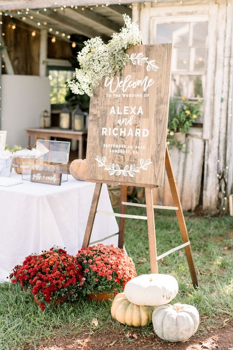 This autumnal welcome sign is adorned with a floral swag of baby's breath and seeded eucalyptus with mums and ornamental pumpkins at the base for a seasonal touch. Photographer Shannon Moffit. Mums Ceremony Decor, White Pumpkins And Eucalyptus Wedding, Mums Wedding Alter, White Mum Wedding Decor, Entryway Wedding Decor Receptions, Mums At Wedding Ceremony, Mums And Pumpkins Wedding, Mums As Wedding Decor, Fall Wedding Mums And Pumpkins