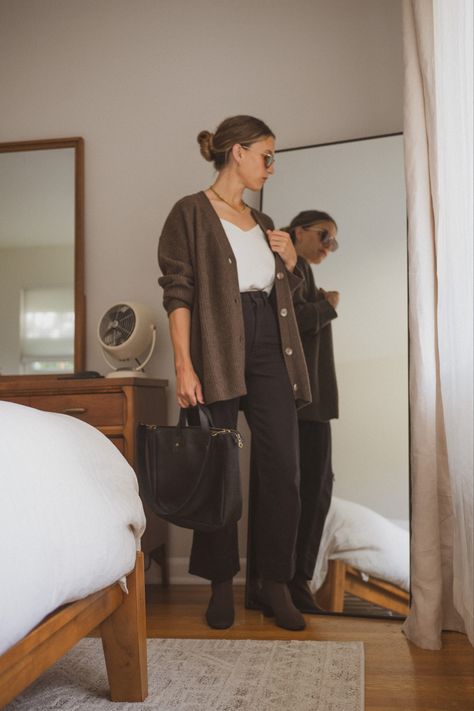 Ashley in her bedroom next to a bed and vintage dresser wearing a white silk cami, chocolate brown oversized cardigan, black cropped pants, brown sock booties, tortoiseshell sunglasses, and a black tote bag Brown Button Up Cardigan Outfit, How To Style A Brown Cardigan, Cardigan Button Up Outfit, Chocolate Brown Cardigan Outfit, Black Outfit Brown Boots, Outfits With Brown Cardigan, Brown Boots With Black Pants, Black Cardigan Outfit Ideas, Dark Brown Cardigan Outfit