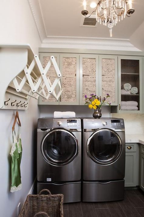 French laundry room features a Paris flea market chandelier illuminating gray cabinets fitted with French script doors suspended over a silver front load washer and dryer. French Laundry Room, Cottage Laundry Room, Perfect Laundry Room, Laundry Room Storage Shelves, Drying Room, Small Laundry Room Organization, Tiny Laundry Rooms, Room Storage Diy, Laundry Design