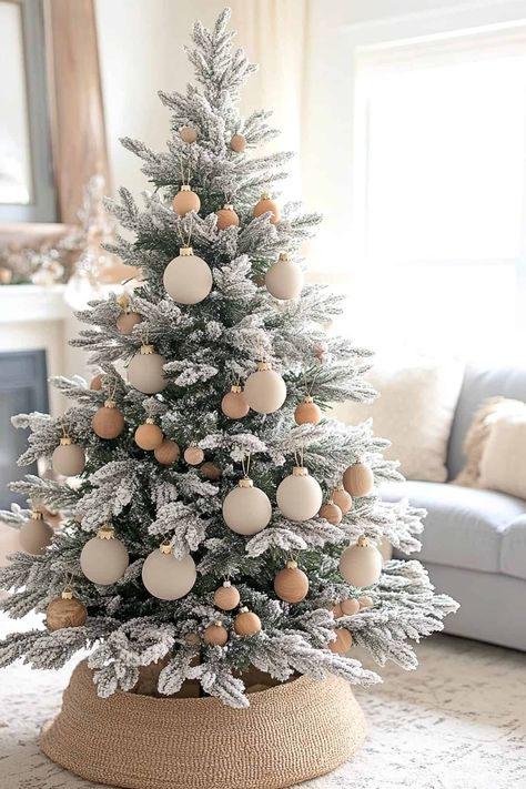 Elegant neutral flocked Christmas tree adorned with white and silver ornaments and twinkling lights. Flocked Christmas Tree Decorated Neutral, Fake Snow Christmas Tree Decorations, Flocked Christmas Trees Decorated Neutral, White Neutral Christmas Tree, Christmas Tree Bottom Ideas, Frosted Christmas Tree Ideas, Flocked Tree Decorating Ideas, White And Silver Ornaments, Beige Christmas Tree