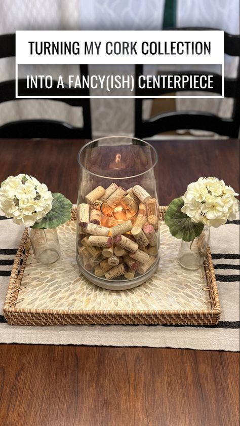 A wicker tray holds a large glass jar filled with wine corks and a candle, with a milk bottle with a sprig of hydrangeas on either side. Wine Cork Vase Ideas, Wine Cork Storage Ideas, Glass Jar Centerpieces, Wine Cork Centerpiece, Wine Cork Storage, Italian Dinner Party Decorations, Cork Candle, Cork Collection, Wine Cork Ideas