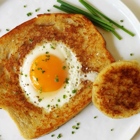 An overhead shot of Eggs in a Basket on a white plate with chives sprinkled on top and some laying the side of the plate. Eggs In A Basket, Breakfast Sausage Recipes, How To Make Eggs, Smothered Chicken, Chewy Peanut Butter Cookies, Bacon Wrapped Chicken, Layered Salad, Quick And Easy Breakfast, Silicone Baking