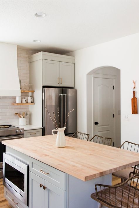 Grey kitchen island with wood butcher block countertop, built-in microwave, and bar stools. Butcher Block Island Gray Cabinets, Kitchen Mood Board Butcher Block, L Shaped Kitchen With Island No Window, Small White Kitchen With Island, Butcher Block Island With Seating, White Kitchen Cabinets With Butcher Block, Butcher Block And Quartz Countertops, Kitchen With Butcher Block Counters, Butcher Block Countertops Kitchen