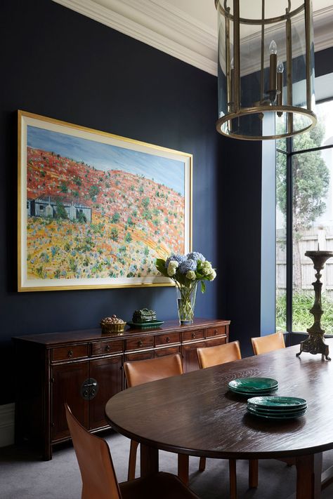 This traditional home was given a colourful makeover! Done by the team at Brownlow Interior Design, this beautifully restored period home was updated using a bold colour palette. This dark blue dining room features a dark wood dining table, leather chairs, green plates, grogeous abstract landscape artwork and a stunning dark brown wood cabinet on the side. To find the full home tour, click on the pin or go to StyleCurator.com.au. Victorian Italianate House, Dark Blue Dining Room, Dark Wood Dining Room, Decorating With Antiques, Italianate House, Georgian Table, Antique Bedside Tables, Dark Wood Dining Table, Maple Dining Table