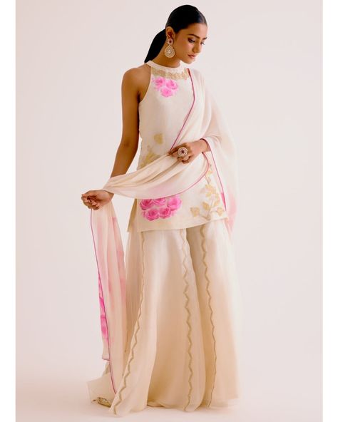 The ivory and pink silk organza sharara set features beautiful floral hand-paint and zari embroidery details over it's short kurta. The outfit is paired with a matching high waisted embroidered sharara and a hand-painted pure georgette dupatta. Indowestern Outfits For Wedding, Hand Painted Outfits, Halter Neck Kurti Designs, Organza Suit Design, Halter Neck Kurta, Halter Neck Kurti, Organza Outfit, Organza Sharara, Kurta Pattern