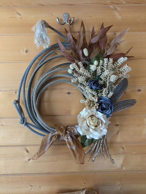 Beautiful western rope wreath/lasso wreath adorned with touches of cowboy brown colors, rustic fall leaves, a bundle of real dried twigs, two turkey feathers, beige and dark blue roses, and a caramel-color bandana to tie it all together. The entire arrangement is supported by a real western rope, once thrown by a mysterious cowboy or cowgirl, chasing rodeo or cattle drive dreams on horseback. Goes great with rustic, farmhouse, country, mountain, and cabin themes, and will serve as an eye-catchin Western Rope Wreath, Western Rustic Home Decor, Lasso Wreath, Cowboy Wreath, Western Wreath, Rope Wreaths, Western Wreaths, Cowboys Wreath, Cowboy Bandana