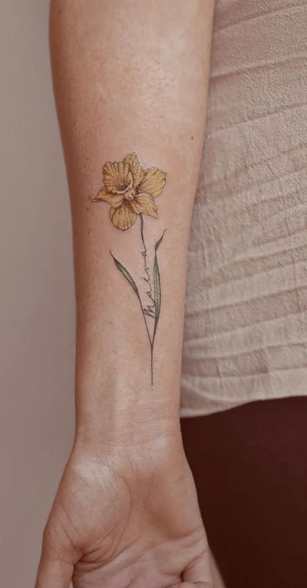 100 Meaningful Daffodil Tattoo Designs - Tattoo Me Now Daffodil Wrist Tattoos For Women, Daffodil With Name Tattoo, Unique Daffodil Tattoo, Daffodil Tattoo With Name In Stem, Colored Daffodil Tattoo, Daffodil Memorial Tattoo, Rose Daffodil Tattoo, Minimalist Daffodil Tattoo, Dafadills Tattoo Design