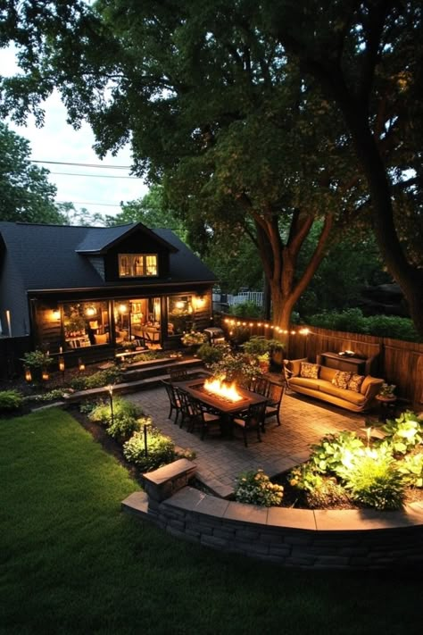 Backyard patio with fire pit, outdoor seating, string lights, and lush garden at dusk. Lounge Backyard Ideas, Small Cozy Garden Ideas, Cozy Private Backyard, Split Backyard Ideas, Backyard Ideas Big Yard, Cozy Backyard Ideas Landscaping, Parklike Backyard, Small Fenced In Backyard Ideas, 1 Acre Backyard Ideas