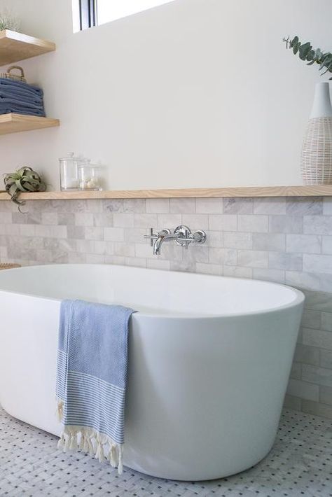 Half marble subway tiled wall in a cottage bathroom completed with a long oak floating shelf over an oval bathtub. Bathroom Trim, Tiled Tub, Master Addition, Tub Design, Oak Floating Shelves, Marble Subway Tiles, Bathtub Walls, Primary Bath, Shower Floor Tile