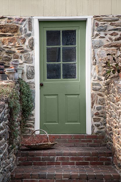 Brick stairs leading up to a green front door surrounded by stacked stone. Yellow Door Green Shutters, Green Front Door Stone House, Front Door Colors With Stone House, Yellow House With Green Door, Dark Gray House With Green Door, Green Paint For Front Door, Brick House With Painted Front Door, Green Front Door Colors With Red Brick, Green Door Cottage