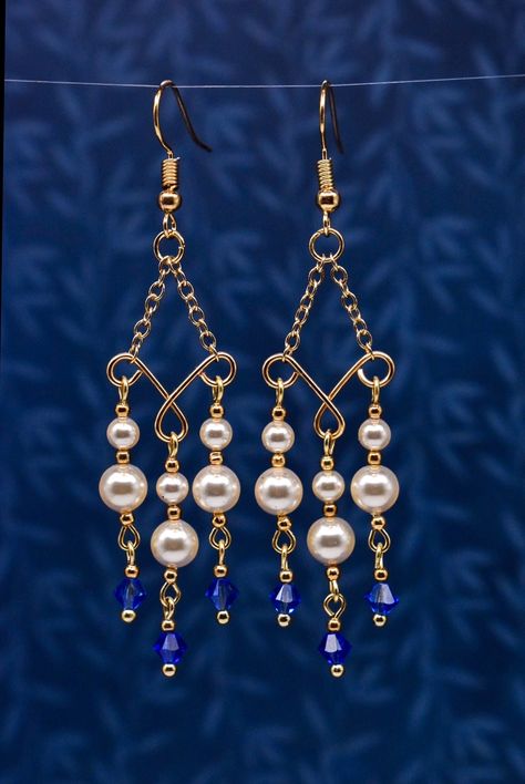 These beautiful earrings combine gold tinted Swarovski pearls with majestic blue bicone crystals to create a sophisticated, elegant pair of earrings that add the perfect finishing touch to your outfit for any special occasion. They come on golden, hypoallergenic ear wires with rubber rubber backs to keep them securely on your ears. They would make a great addition to your own collection, or a beautiful gift for a loved one! Diy Earrings Pearl, Simple Bead Earrings, Wire Jewelry Earrings, Beaded Earrings Diy, Earrings Chandelier, Wire Jewelry Tutorial, Wire Jewelry Designs, Unusual Earrings, Diy Wire Jewelry