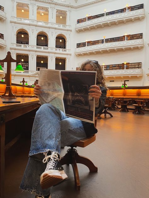 Girl is sitting in the state library of Victoria holding a newspaper and reading it. She has blonde curly hair with black glasses on her head. She is also wearing blue jeans and converse State Library Victoria, Studying Photoshoot, Library Photoshoot Ideas, Victoria Aesthetic, Library Shoot, Library Photoshoot, Library Photo Shoot, State Library Of Victoria, Aesthetic Library