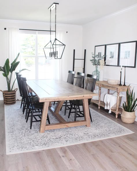 Light wood dining table is accented with black spindle back dining chairs under a black linear lantern light. Gray and beige vintage area rug for kitchen table is laid underneath the table covering stained wood flooring. Dining Table With Grey Floor, Light Table Dark Chairs Dining Room, Dining Table With Black Spindle Chairs, Light Gray Rug Living Room, Dining Room Table With Grey Floors, Light Wood Flooring Dining Room, Rug Under Dining Table Or Not, Rug Under Long Dining Table, Grey Wash Dining Table With Black Chairs