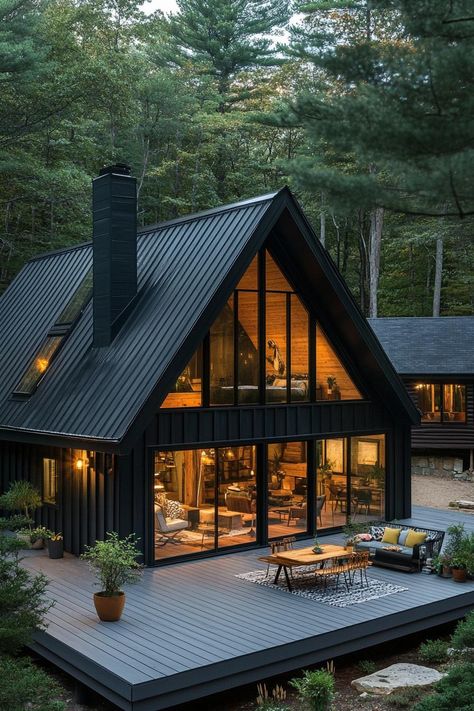 Modern black a frame house with black board and batten siding black metal roof with chimney a gambrel with window on the roof side large glass. Check out all of these stunning and chic dark A-frame houses that pack a ton of charm into a small forest retreat. A Frame With Fireplace, Black A Frame House Exterior, Black And White A Frame House Exterior, Black Board And Batten Siding, Black A Frame House, A Frame Barndominium, Metal Board And Batten Siding, A Frame Cabin With Addition, Black A Frame