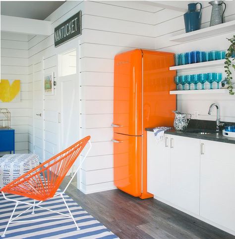 Well decorate orange and blue sunroom is fitted with an orange Smeg refrigerator placed against a white tongue and grove wall beside white floating shelves. Colorful Kitchen Appliances, Beach Style Kitchen, Tongue And Groove Walls, Smeg Fridge, White Floating Shelves, Vintage Stoves, Colorful Kitchen, Cottage Living Rooms, Cottage Kitchens