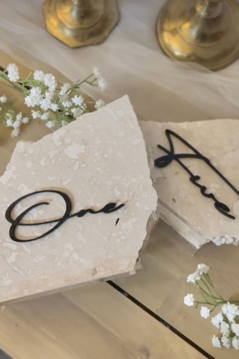 Acrylic clear bases, travertine, and black acrylic lettering. Stone Themed Wedding, Table Numbers Wedding Stone, Stone Seating Chart, Stone Wedding Table Numbers, Fabric Table Numbers, Diy Stone Table Numbers, Rock Table Numbers, Marble Table Numbers, Travertine Table Numbers