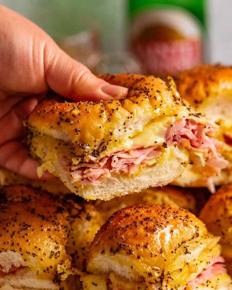 Hand holding Hot Ham and Cheese Sliders Ham Biscuits With Hawaiian Rolls, Ham And Cheese Baked, American Food Party, Hot Ham And Cheese Sliders, Hot Ham And Cheese, Soft Rolls, Ham And Cheese Sliders, Seasoned Butter, Cheese Sliders