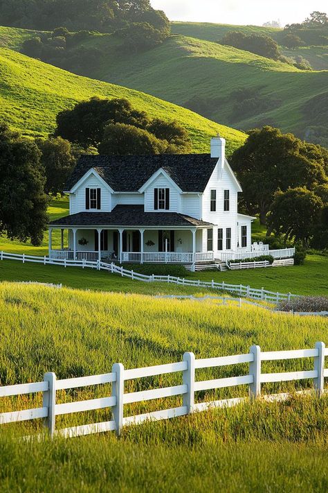 White farmhouse with a wraparound porch in lush hills. Imagine sipping lemonade on a wrap-around porch that overlooks fields of gold and a barn so grand it almost demands its own Christmas lights! White House On A Hill, House With A Wrap Around Porch, White House With Wrap Around Porch, White House Wrap Around Porch, Farmhouse With Porch, Farmhouse Ranch Style Homes, Wraparound Porch Farmhouse, North Carolina Houses, House Exterior Garden