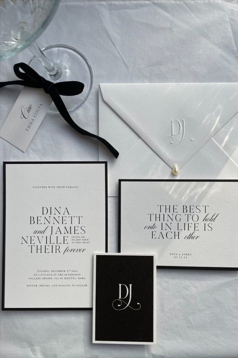 A stylish wedding stationery suite displayed on a white surface, featuring a black and white theme. The set includes a wedding invitation, a card with a romantic quote, a monogrammed envelope adorned with a small pearl, a personalized place card tied with a black velvet ribbon, and a small black card with a “DJ” monogram. The design emphasizes classic typography, minimalist elegance, and a sophisticated aesthetic, perfect for a luxurious wedding look. White And Black Invitations, Modern Chic Wedding Invitations, Wedding Invitation Stack, Black And White Invitations Wedding, Old Money Wedding Invitations, Black And White Wedding Invites, Wedding Invite Inspiration, Elegant Wedding Invitations Classy, Wedding Invitations Black And White